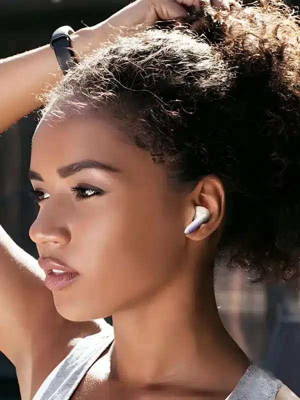Una joven de cabello rizado y pulsera de actividad se ajusta la coleta. Lleva audífonos inalámbricos con doble micrófono ENC Usams, y la luz del sol ilumina su rostro mientras mira a lo lejos.