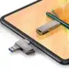 La Memoria USB Usams 16GB Tipo-C USB 3.0 – Transferencia Rápida y Segura, con conectores duales USB-A y USB-C, descansa junto a su tapa sobre una tableta, mientras un teléfono inteligente se observa al fondo.