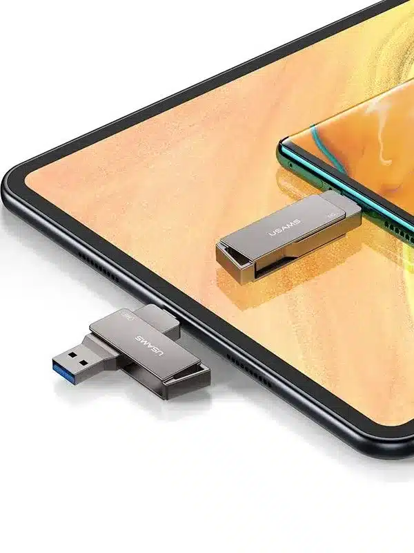 La Memoria USB Usams 16GB Tipo-C USB 3.0 – Transferencia Rápida y Segura, con conectores duales USB-A y USB-C, descansa junto a su tapa sobre una tableta, mientras un teléfono inteligente se observa al fondo.
