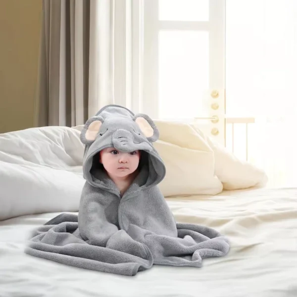 Bebé sentado sobre una cama envuelto en una toalla gris con capucha de elefante.